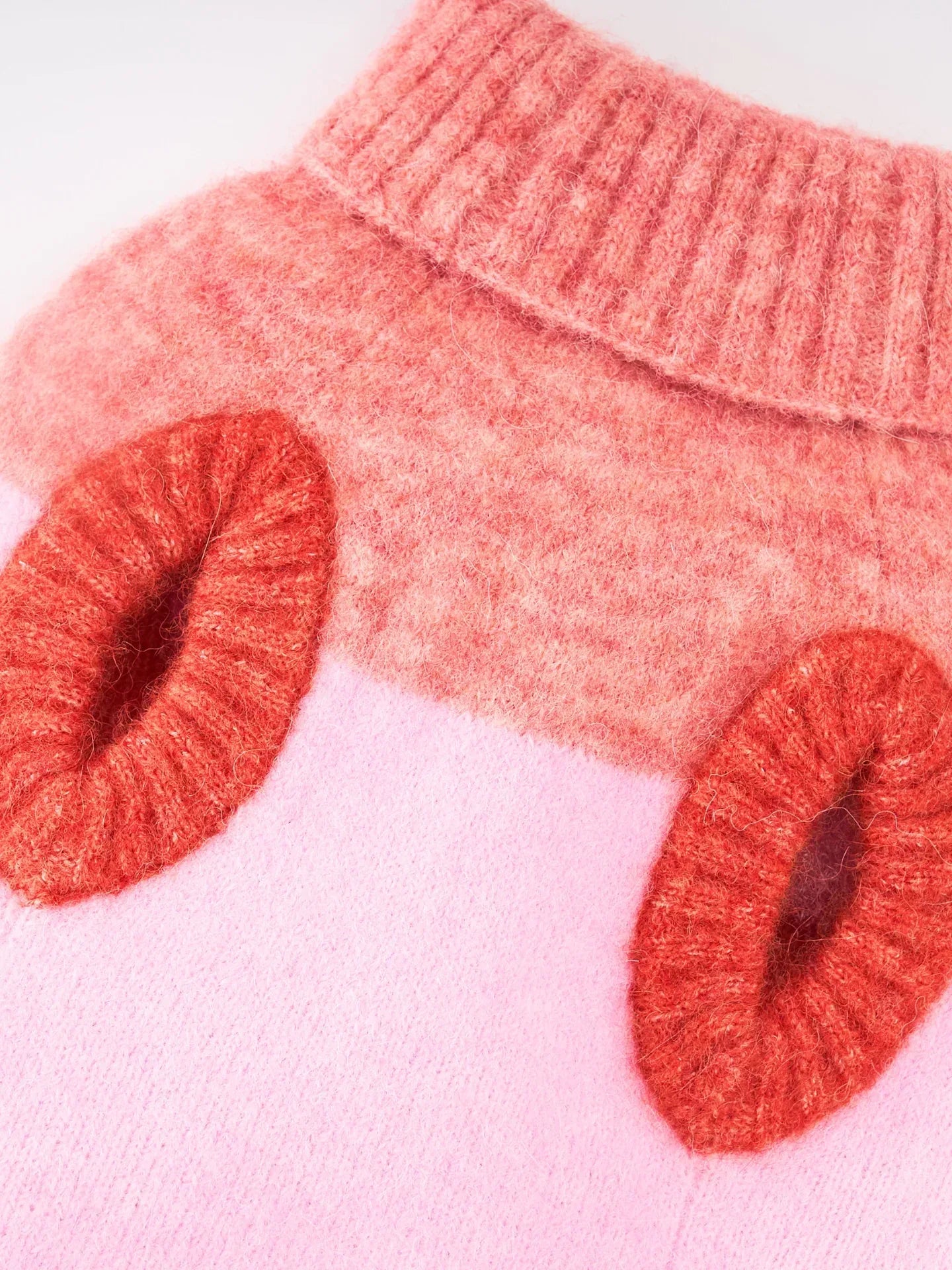 Detailed shot of the comfortable armhole and ribbed trim of the pink and coral red pet knit vest.