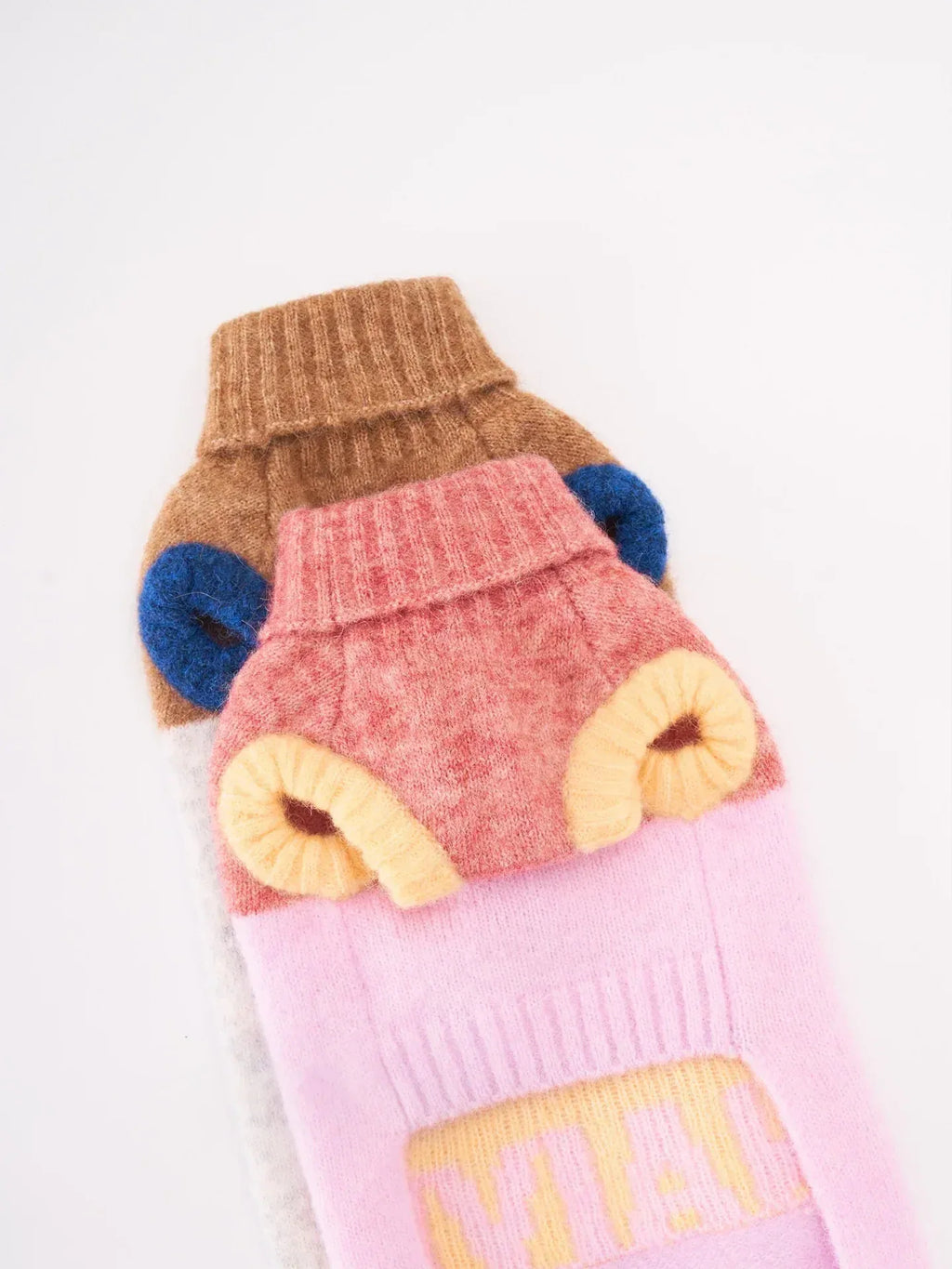 A stack of alpaca wool pet knit vests showing the Pink / Butter Yellow version layered with other series colors.