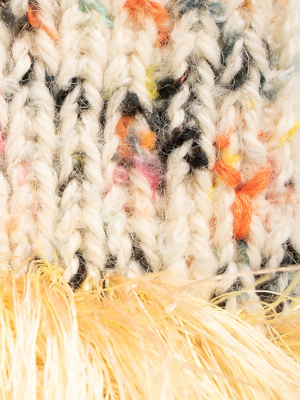 Close-up of the chunky cream speckled wool knit and the multi-colored champagne and bright yellow fringe yarn texture.