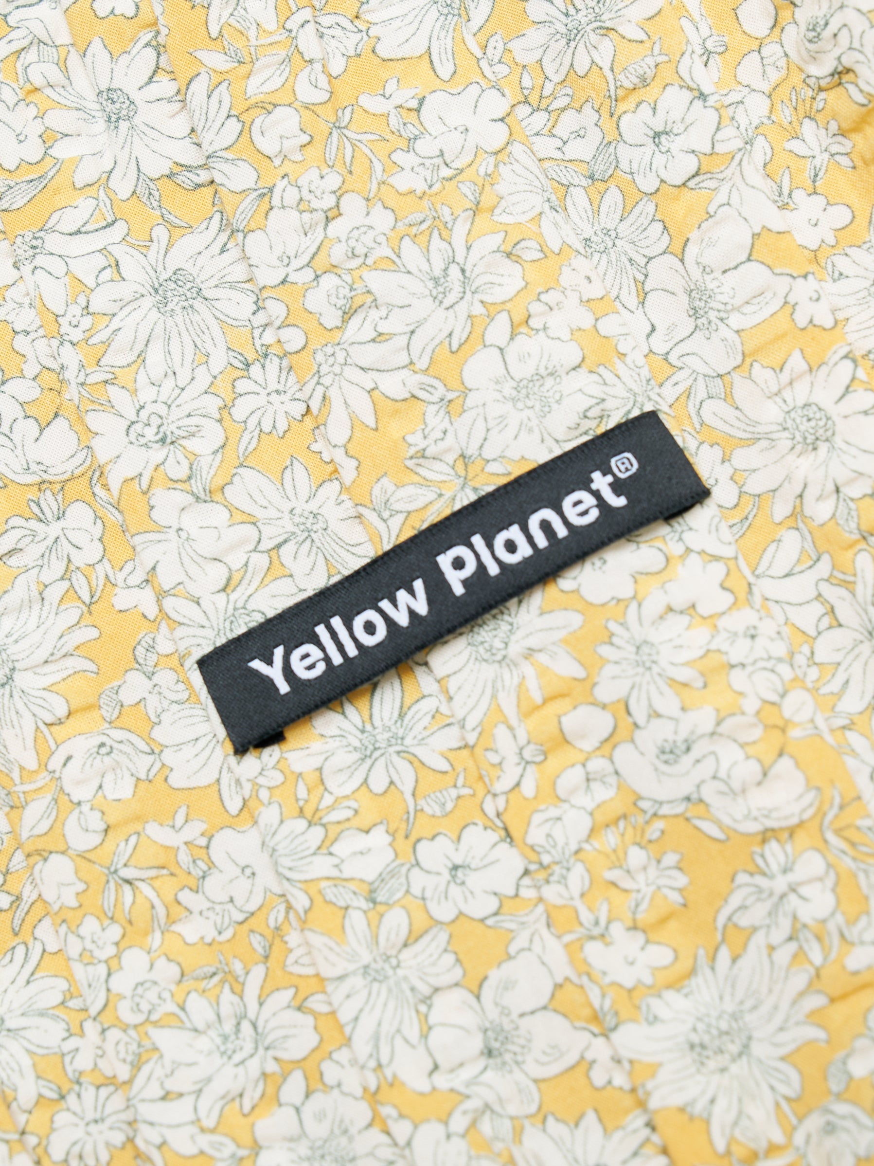 Close-up of the Colorful Daily Nature's Verse Gentle Wave Snood in Daisy showing the floral printed fabric and Yellow Planet label.