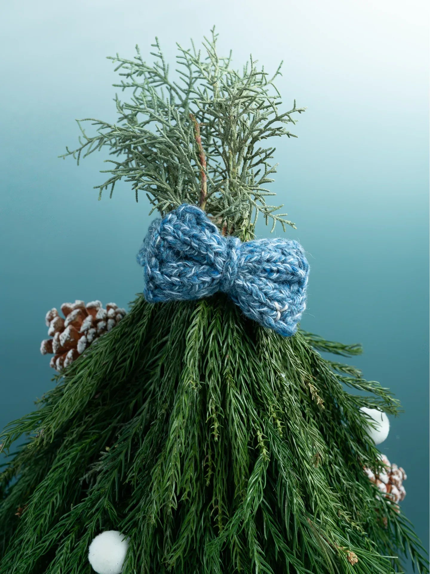 The Denim Tweed knitted bow tie styled as a festive topper on a small evergreen tree.