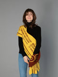 A woman modeling the DOG-Sophy "WOOF" theme reversible scarf in warm yellow and brown, draped over a black turtleneck.