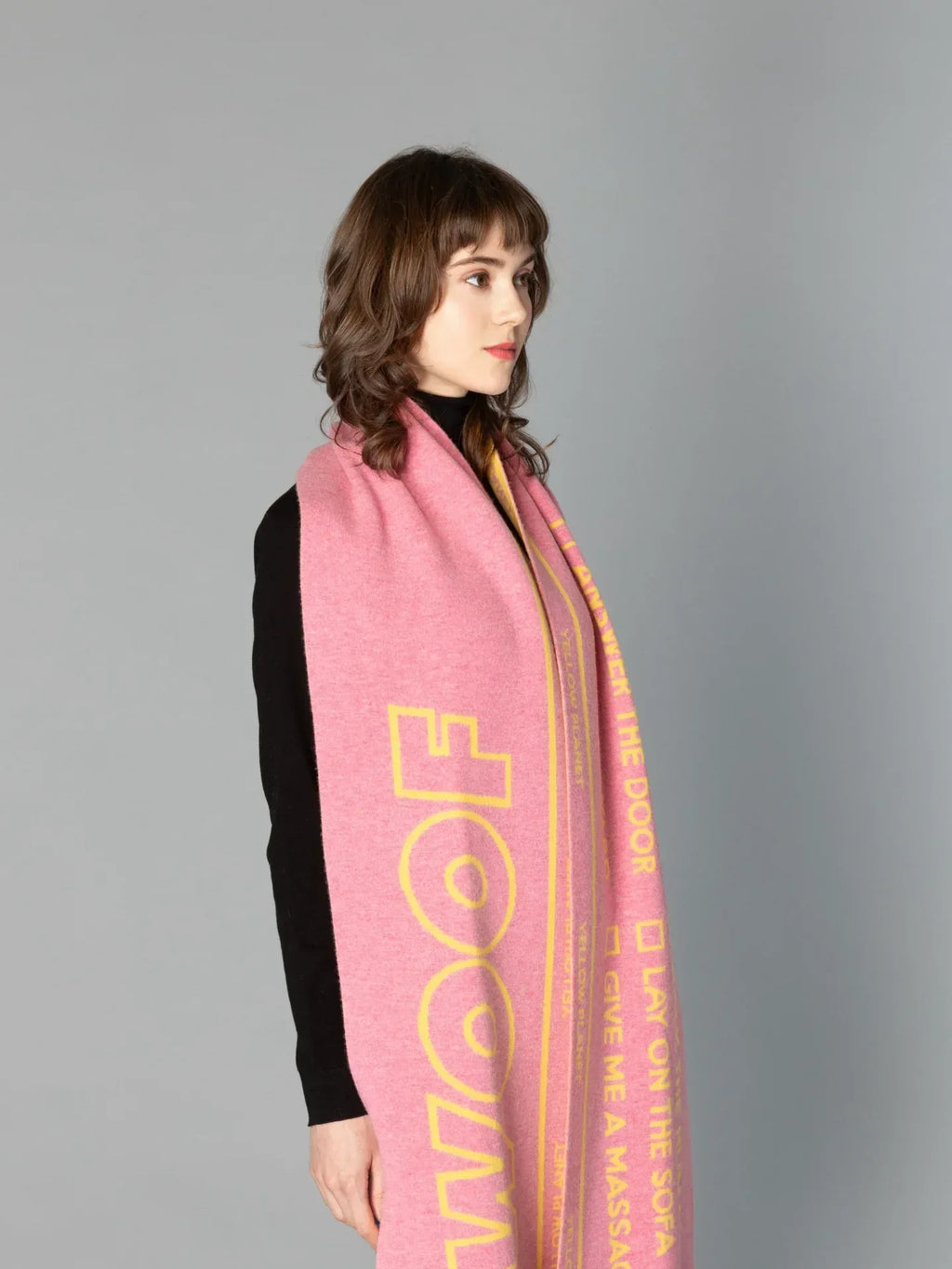Side view of a woman modeling the DOG-Sophy "WOOF" theme reversible wool scarf in a vibrant pink and yellow colorway.