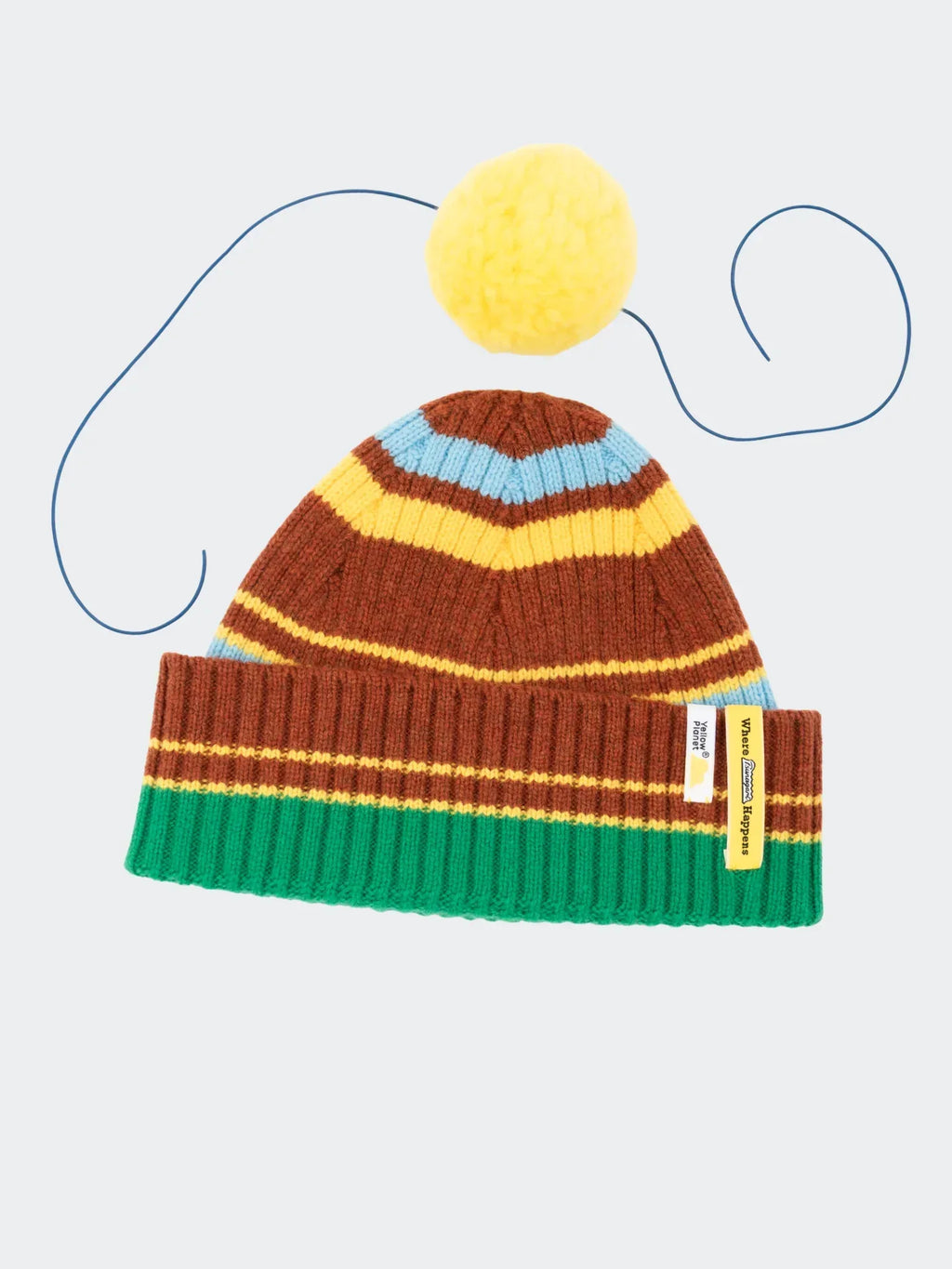 Studio flat-lay showing the striped wool beanie and the separate yellow pom-pom to highlight the detachable feature.