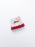 Main studio shot of the limited edition "camellia rose" hand-knitted luxe pet snood in cream speckled wool with wine red fringe tassels.