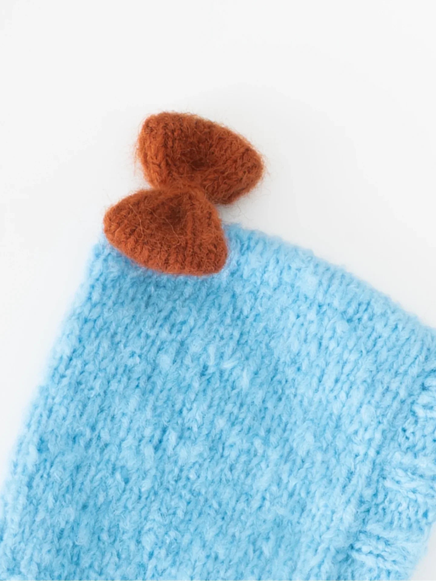 Close-up shot of the hand-knitted caramel brown bow accent on the crown of the sky blue wool pet beanie.