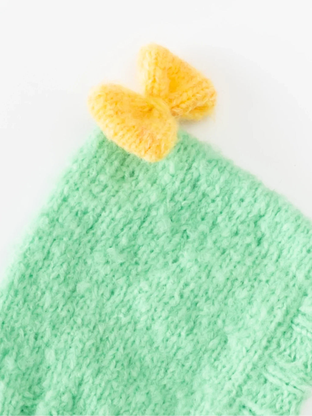 Close-up of the hand-knitted warm yellow bow attached to the crown of the mint green wool pet beanie.