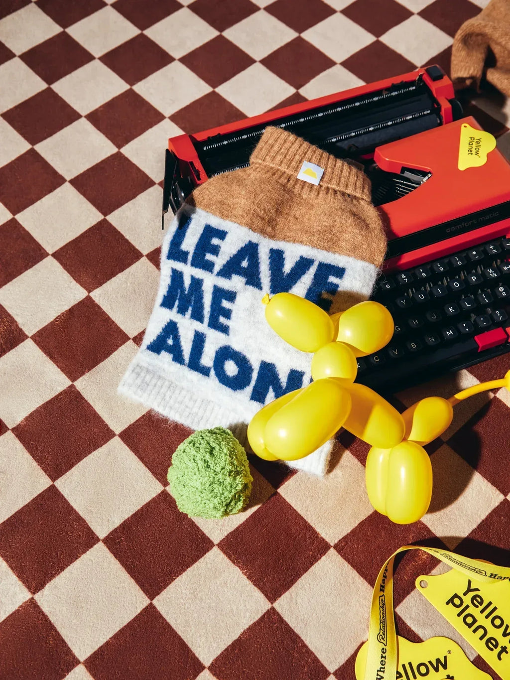 Creative flat lay of the beige gray alpaca wool pet vest with "Leave Me Alone" typography, styled with a yellow balloon dog.