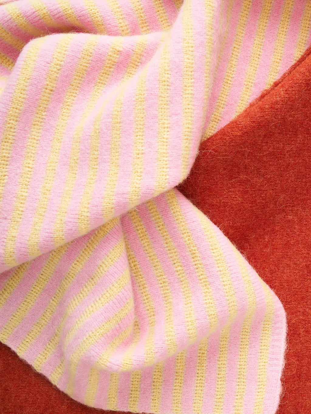A detailed shot of the scarf’s fabric folds, highlighting the contrast between the solid brick red and the striped yellow-pink alpaca blend.