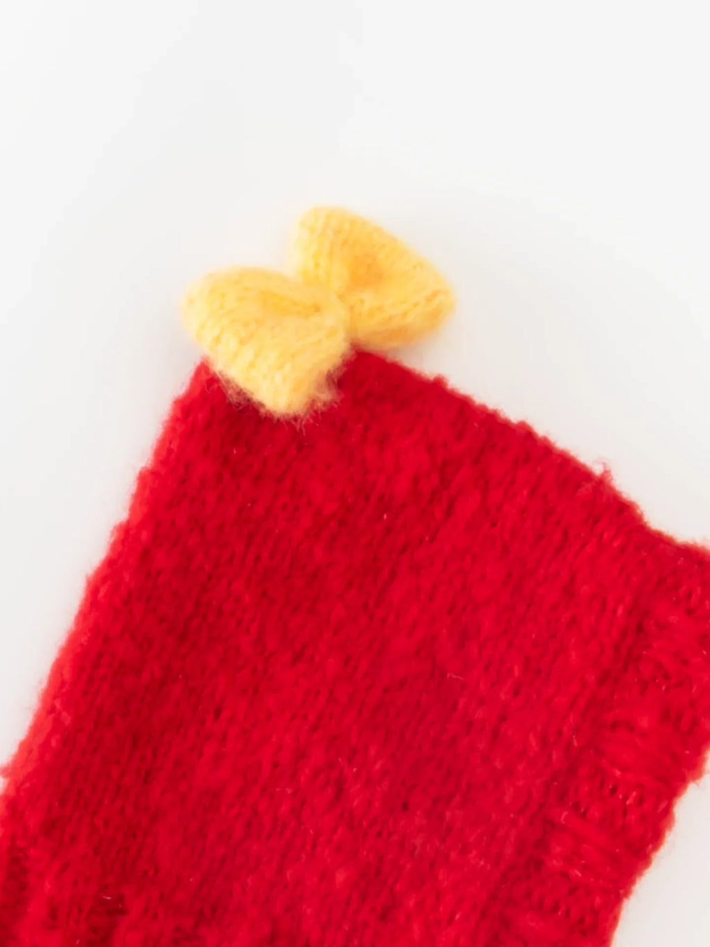 Close-up of the pastel yellow hand-knitted bow attached to the top of the red wool pet beanie.