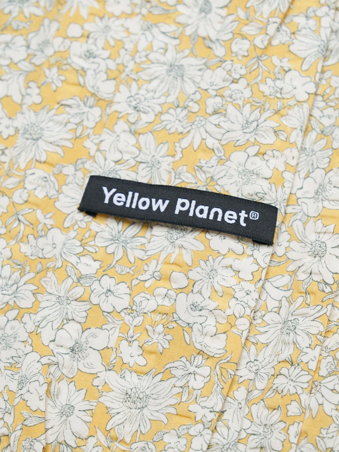 Close-up of the Daisy printed crinkled cotton fabric and Yellow Planet label on the Gentle Wave dog ear snood.