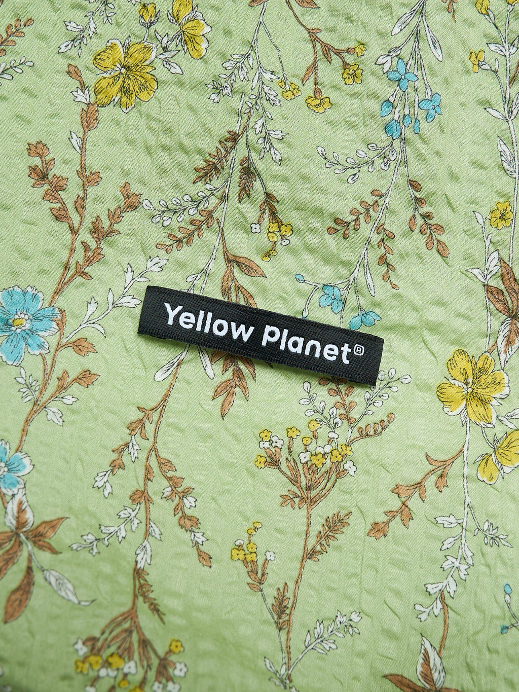Close-up of the Forest Green printed crinkled cotton fabric and Yellow Planet label on the Gentle Wave dog ear snood.