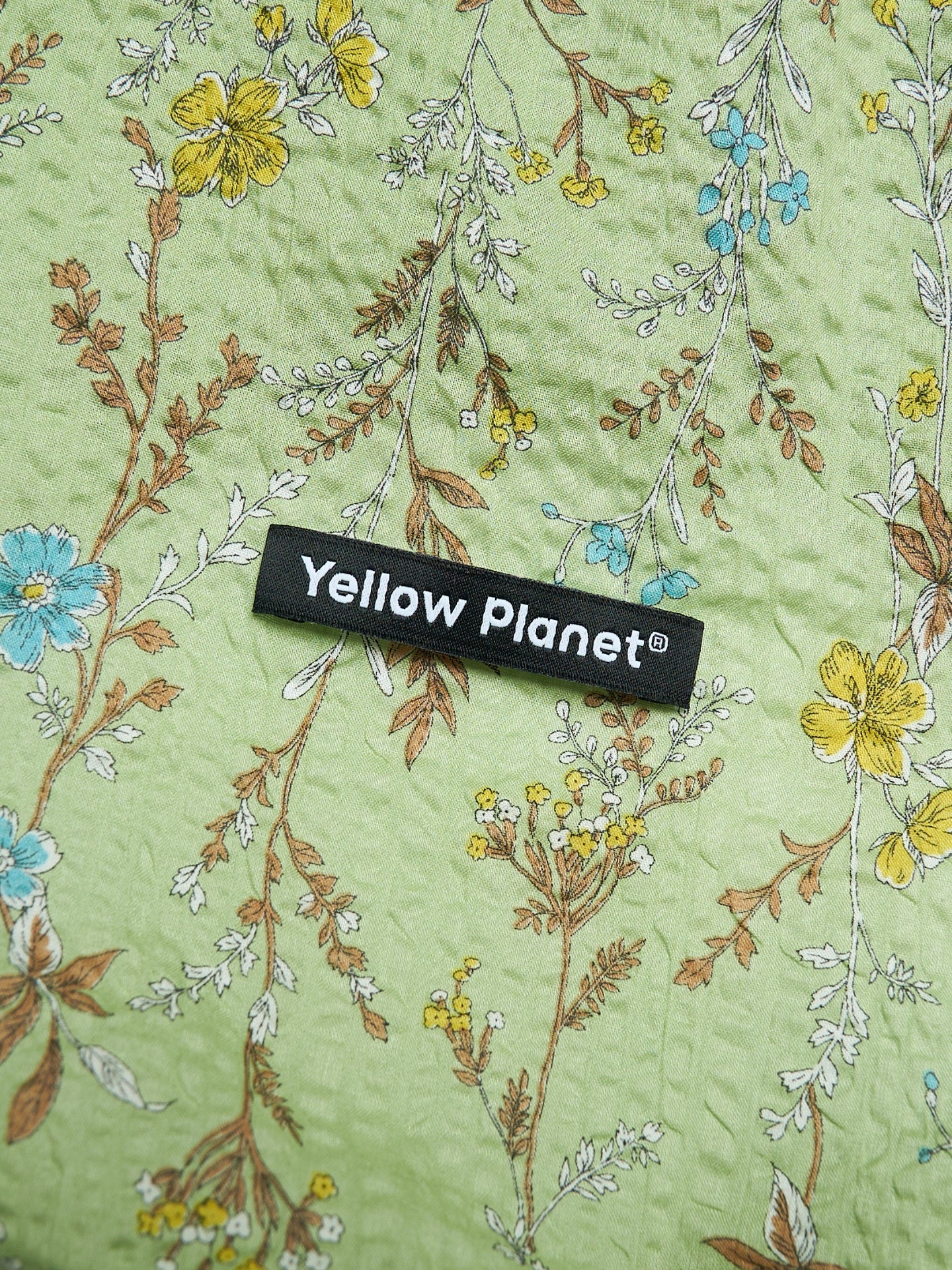 Close-up of the Forest Green printed crinkled cotton fabric and Yellow Planet label on the Gentle Wave dog ear snood.
