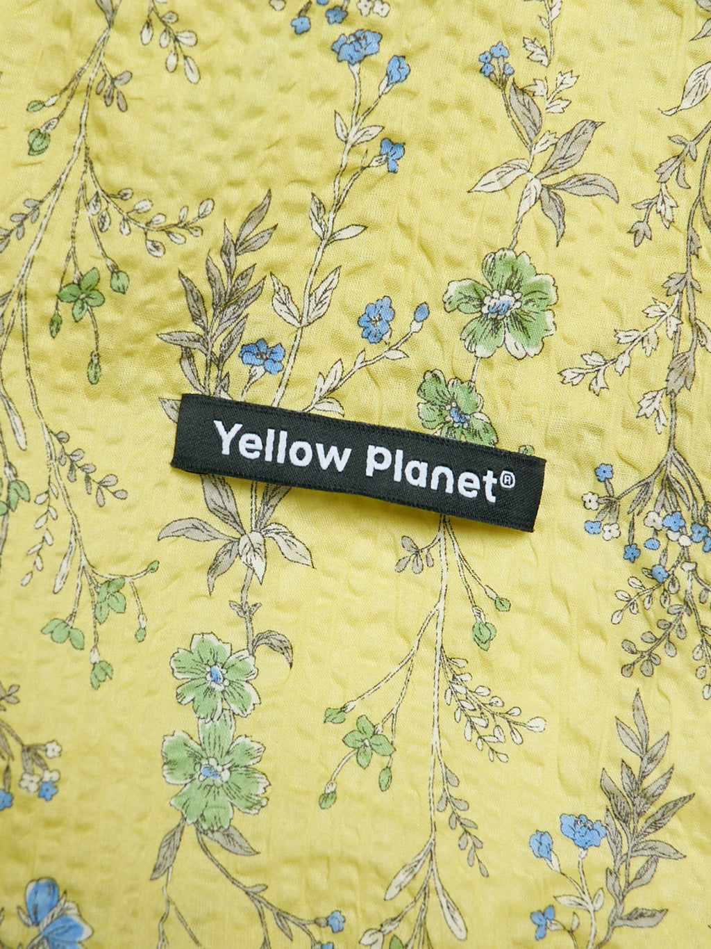 Close-up of the Forest Yellow printed crinkled cotton fabric and Yellow Planet label on the Gentle Wave dog ear snood.