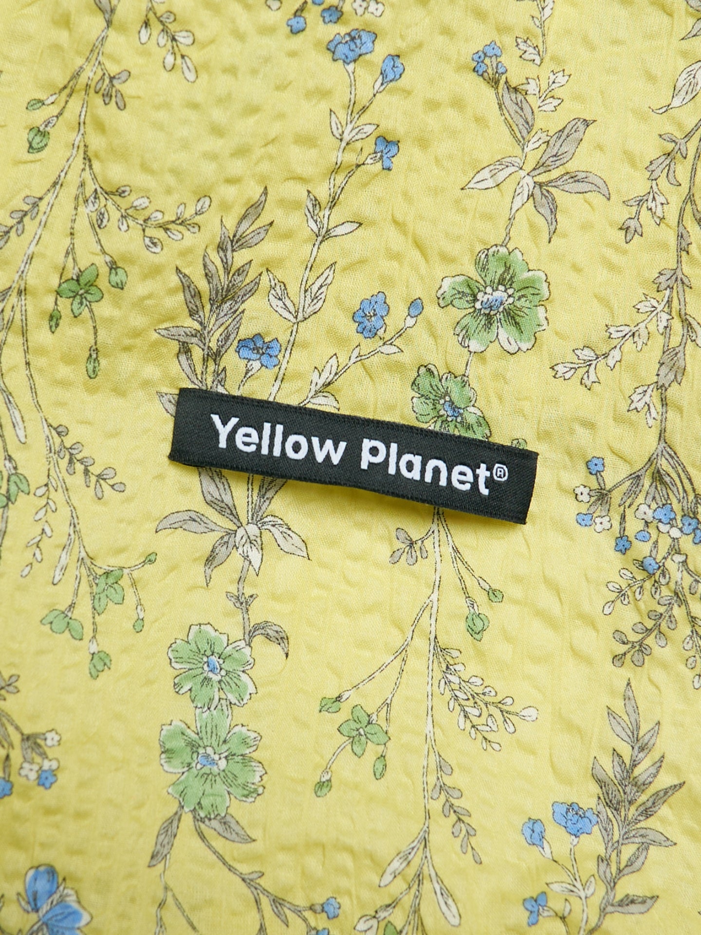 Close-up of the Forest Yellow printed crinkled cotton fabric and Yellow Planet label on the Gentle Wave dog ear snood.