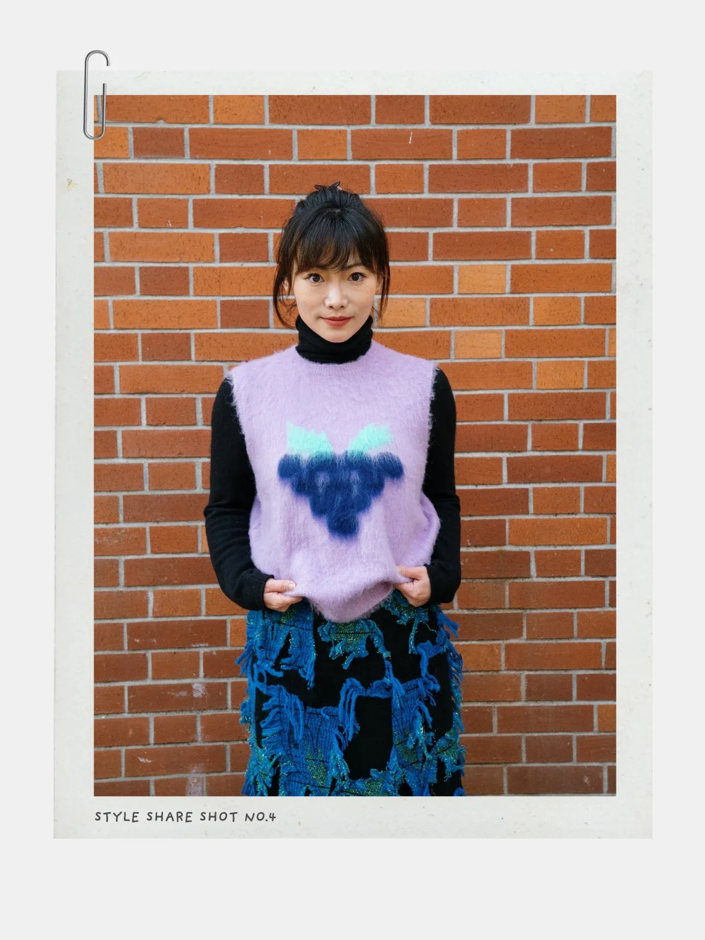 Front view of a model wearing the Night Grape artistic fruit vest standing against a classic red brick wall.
