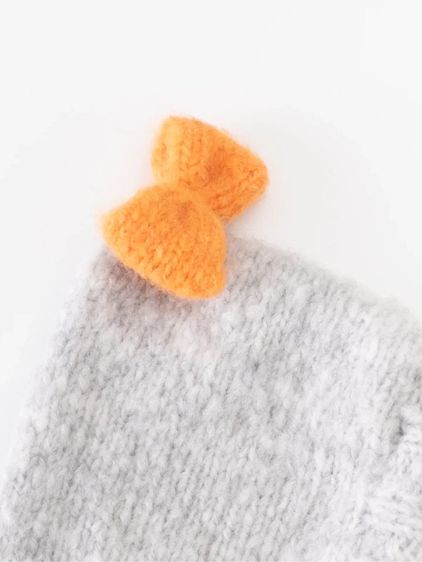 Detailed shot of the hand-knitted orange bow accent on the top of the gray wool pet snood.
