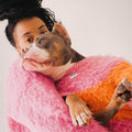 A woman wearing the Pink-Orange brushed knit sweater while hugging her dog, who is wearing the matching pet version of the Fuwa Fuwa series.