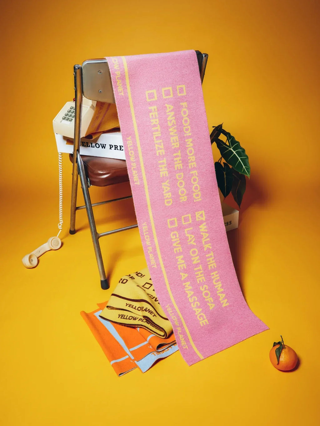 Creative studio display of the pink and yellow "WOOF" scarf on a chair, highlighting the full checkbox design.