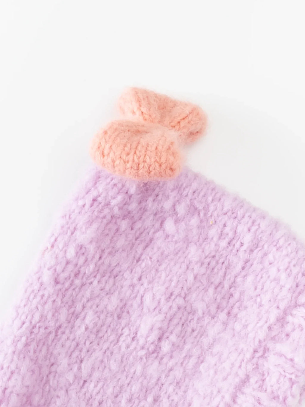 Close-up of the hand-knitted salmon pink bow (BonBon) detail attached to the soft lavender wool pet beanie.