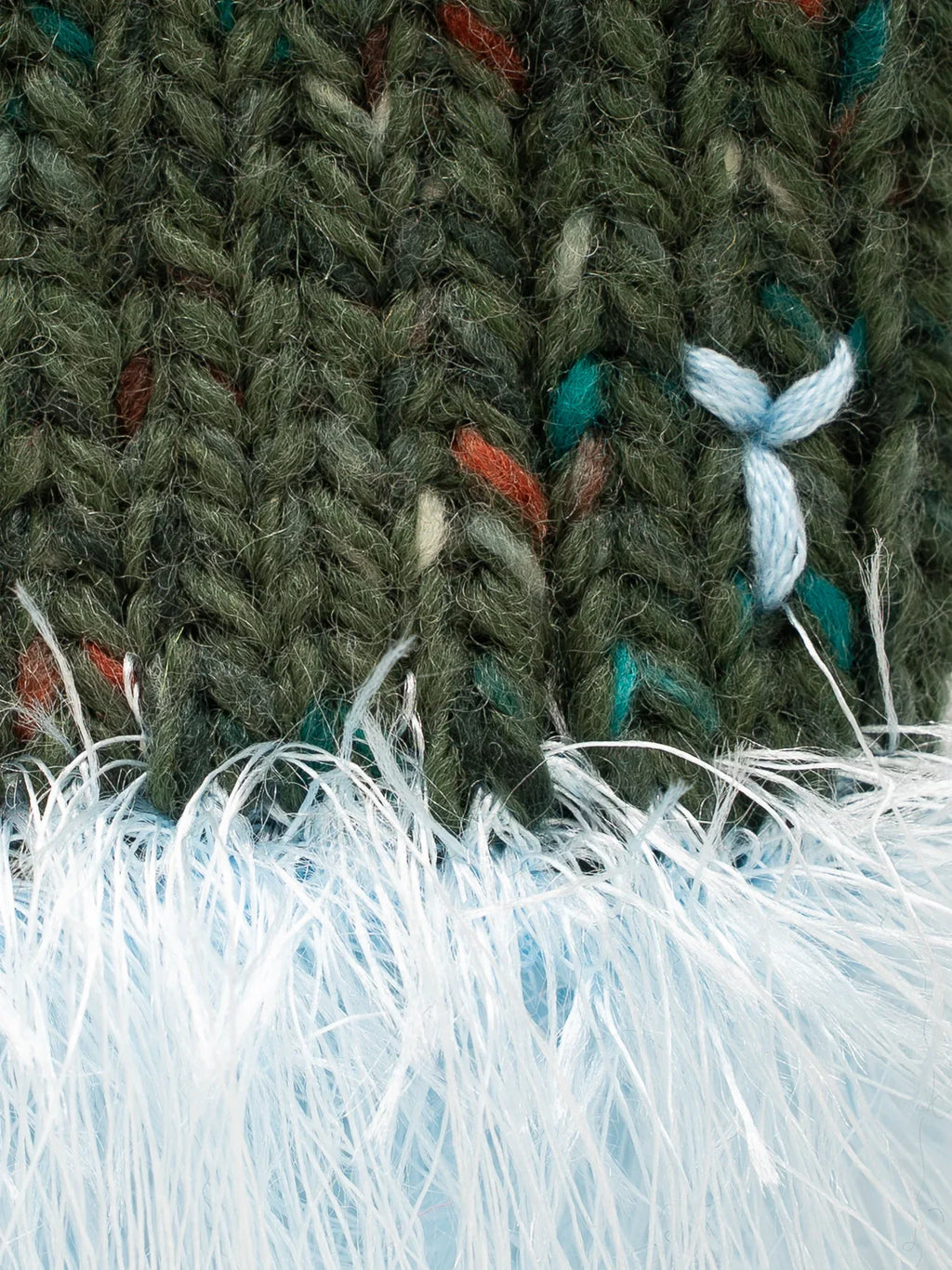 Close-up of the textured olive green speckled wool and the fluffy light blue sea anemone yarn fringe detail.
