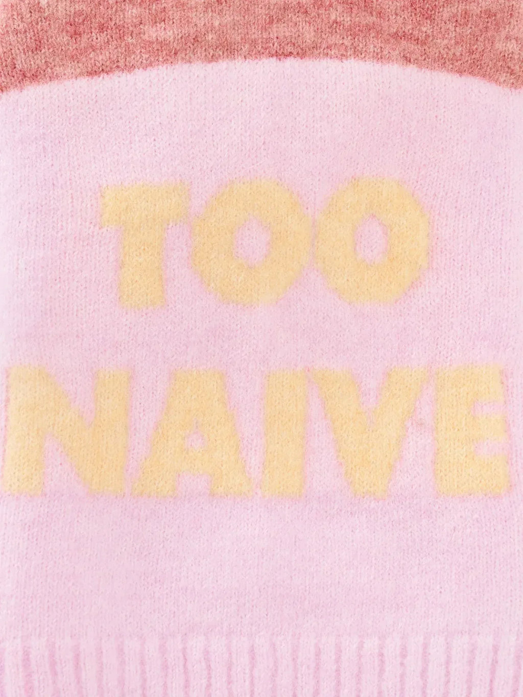 Close-up of the "TOO NAIVE" butter yellow typography on the pink alpaca wool knit fabric.