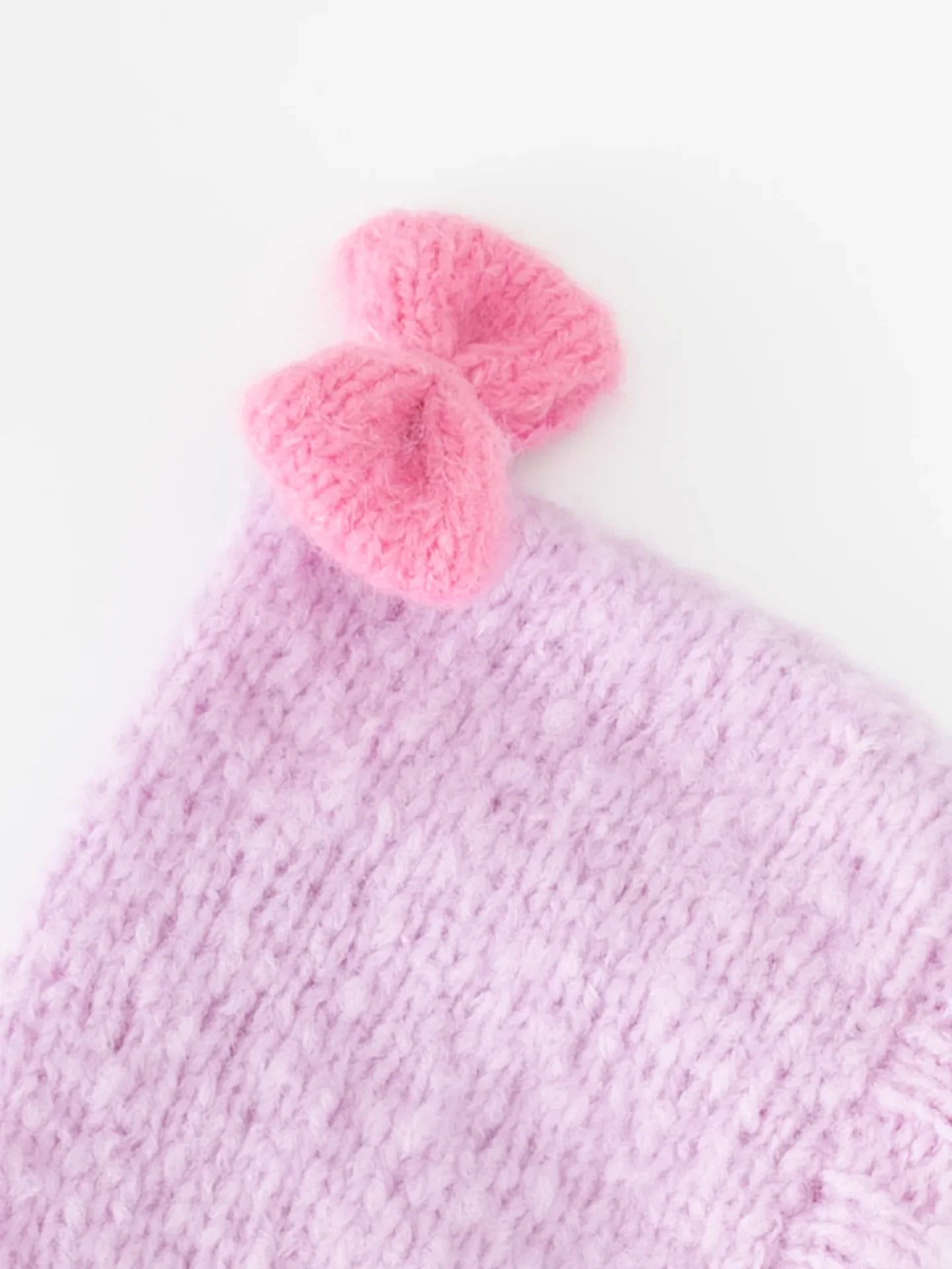 Close-up shot of the hand-knitted vibrant pink bow attached to the top of the lavender wool pet beanie.
