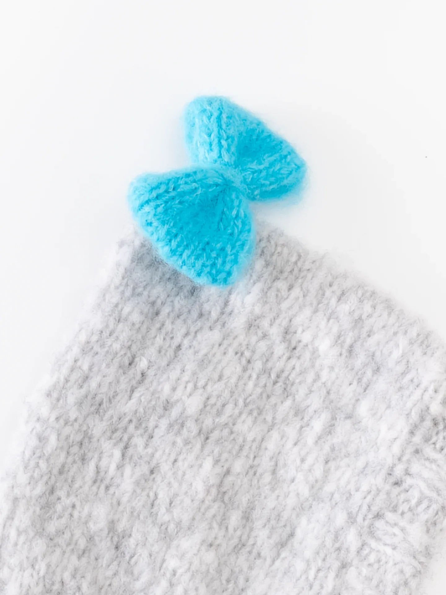 Close-up shot of the artisanal hand-knitted vivid blue bow attached to the crown of the smoke gray wool pet beanie.