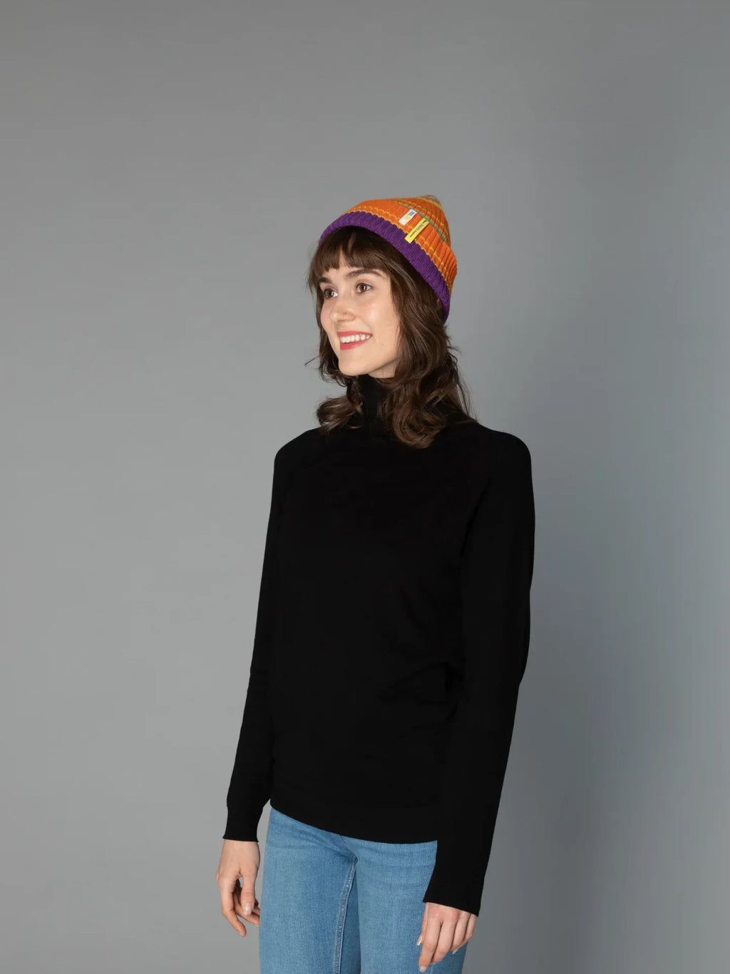 A woman modeling the Vibrant Orange striped wool beanie, highlighting the cuffed ribbed texture and snug winter fit.
