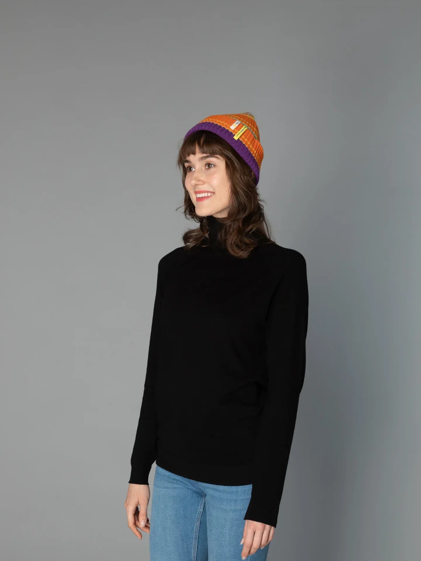 A woman modeling the Vibrant Orange striped wool beanie, highlighting the cuffed ribbed texture and snug winter fit.