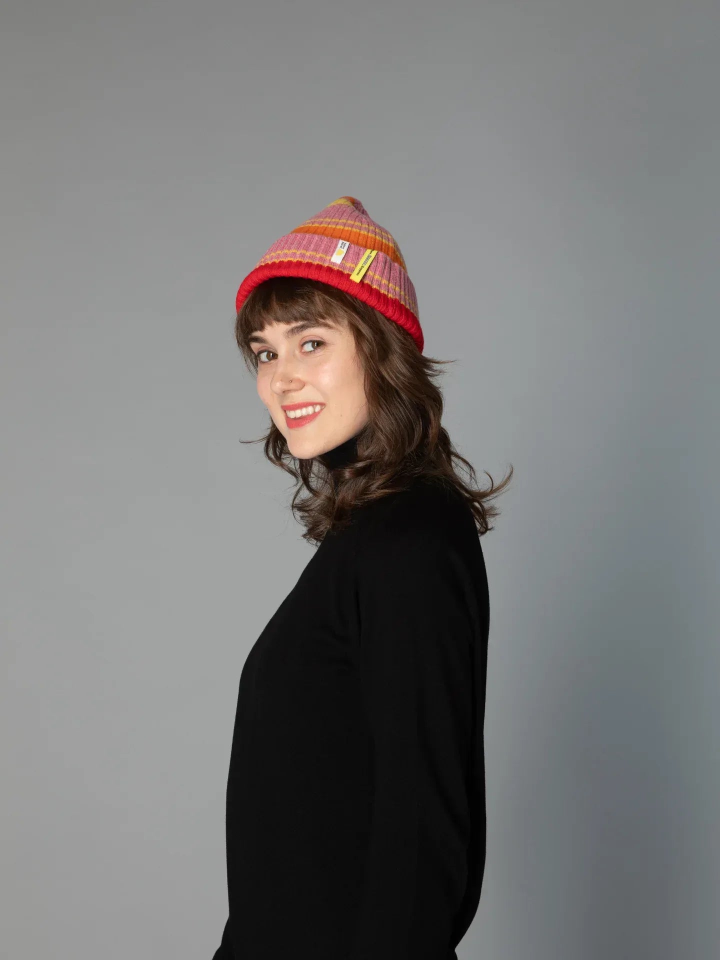 Profile view of a woman wearing the Pink Stripes wool beanie, showcasing the comfortable cuffed fit and bold colors.