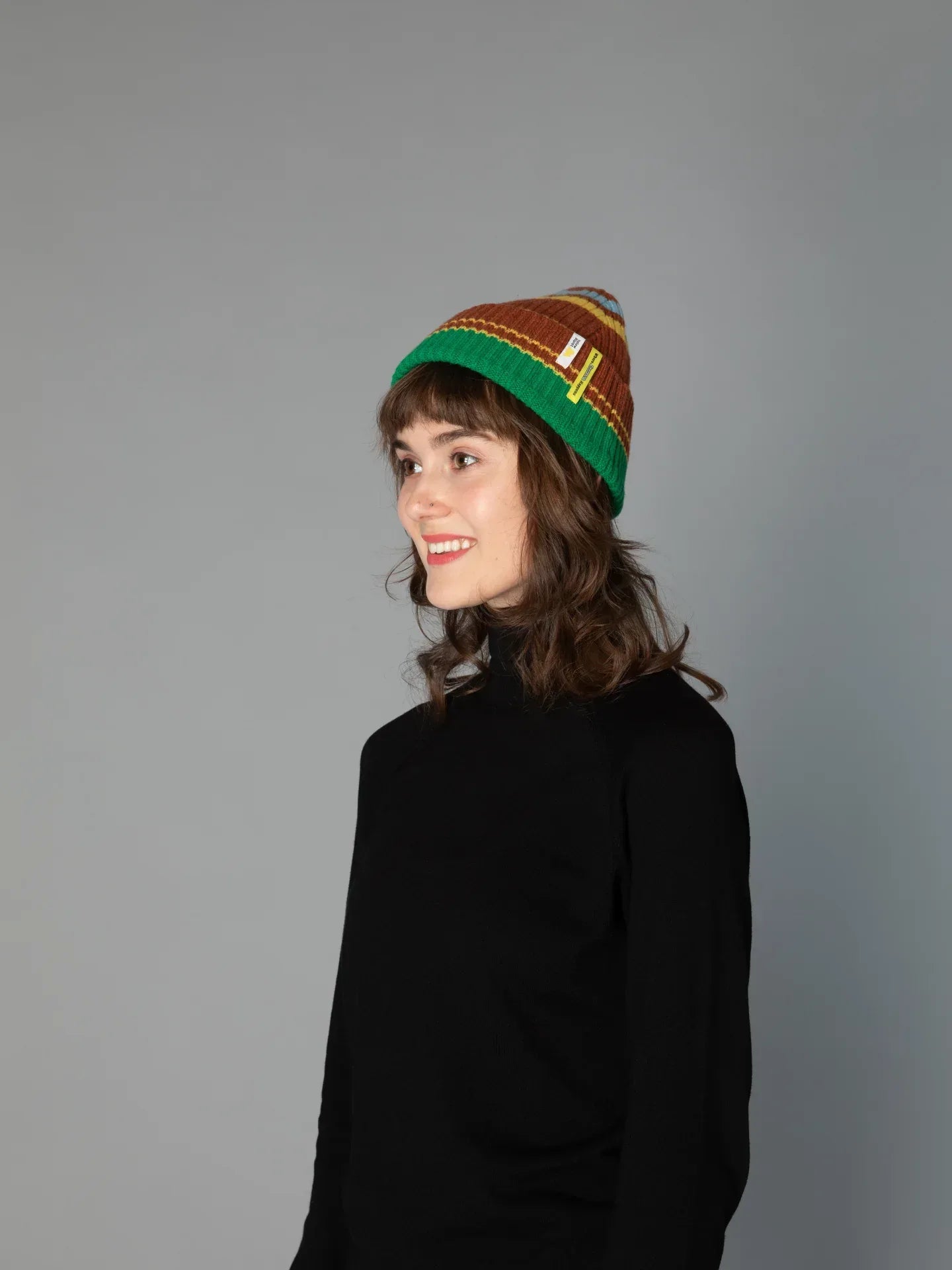 A woman modeling the Chestnut Brown striped beanie without the pom-pom, showcasing a sleek, cuffed winter look.