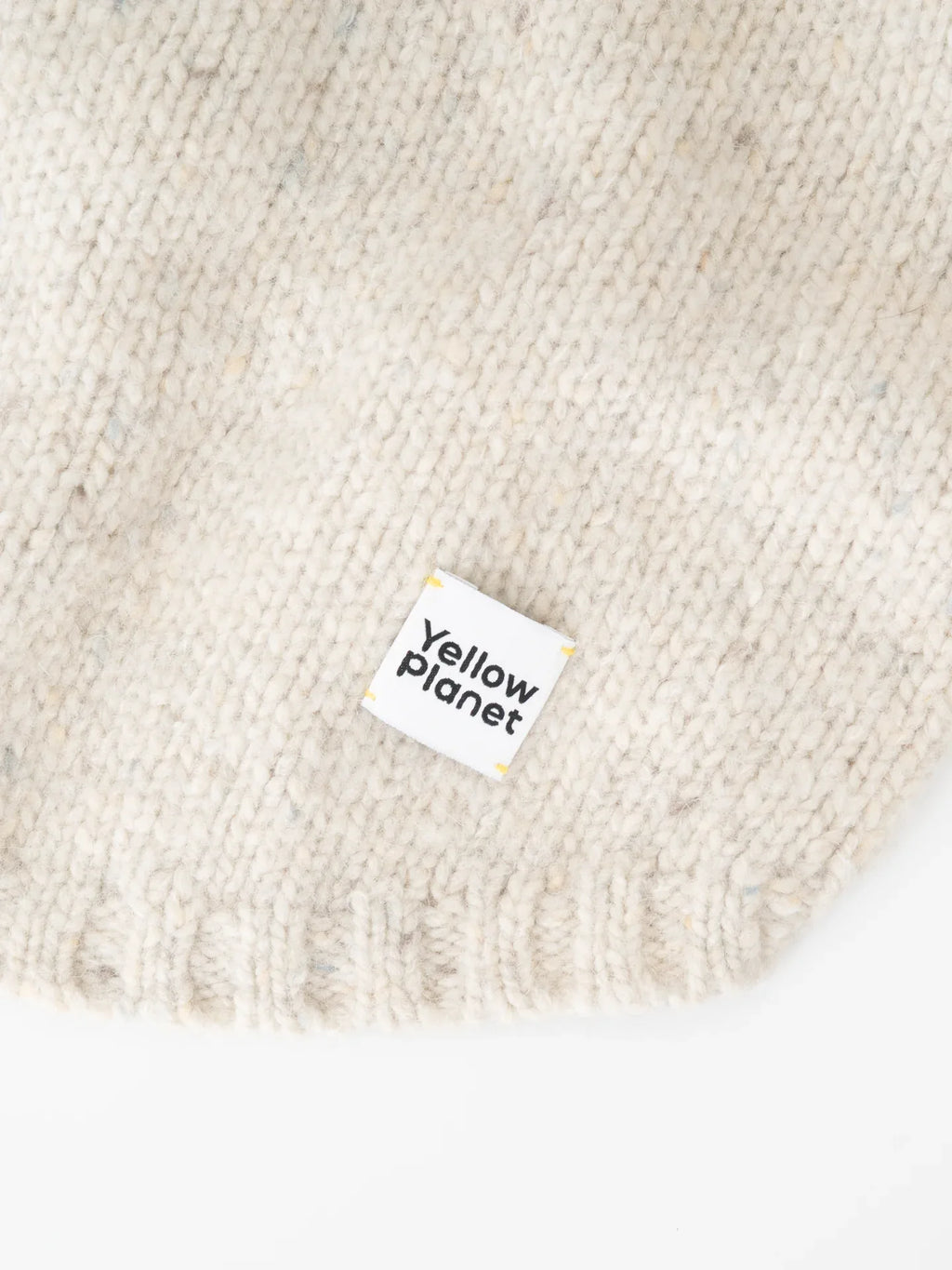 Detailed shot of the "Yellow Planet" woven brand label stitched onto the hem of the Milk Tweed pet sweater.