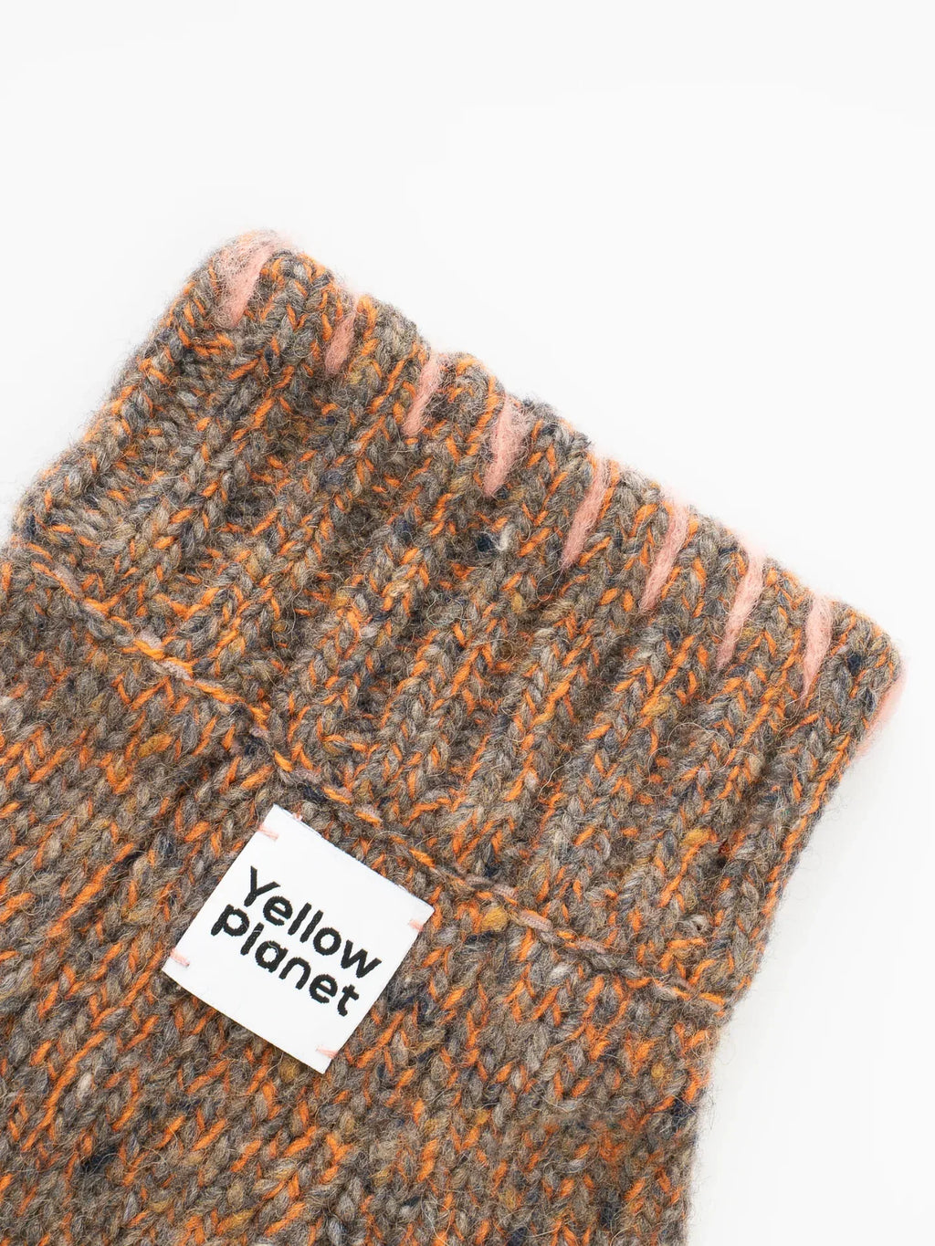 Macro shot of the "Yellow Planet" woven brand label on the ribbed cuff of the Rust Tweed alpaca-wool pet sweater.